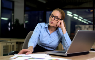 Mujer reflexionando en su puesto de trabajo frente al ordenador, ilustrando la insatisfacción laboral